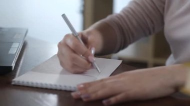 Ofiste dizüstü bilgisayarda çalışan güzel bir genç kız. İş kadını bir not defterine bir kalemle veri yazar ve bilgisayarda metni yazdırır. Ev işleri kavramı. Web mağazası. çevrimiçi