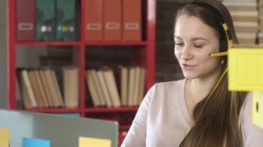 Serbest çalışan kız bir ofiste oturmuş kulaklıklarla bilgisayarda video konferansında konuşuyor. Masada bir sürü dosya var. İş görüşmeleri başlatıldı. Merkez ofiste uzaktan çalışma.