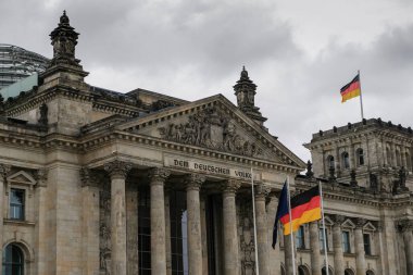 Berlin 'in ünlü tarihi Reichstag cephesi Bulutlu gökyüzünde Alman bayrakları, sembol