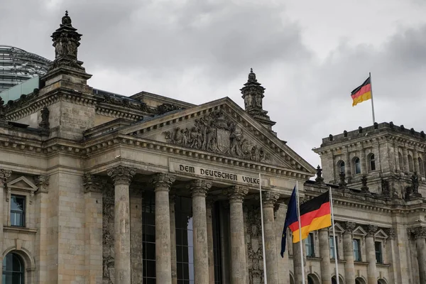Berlin 'in ünlü tarihi Reichstag cephesi Bulutlu gökyüzünde Alman bayrakları, sembol