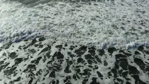 Vzdušné létání zpět pohled přes stříkající vlny pohyb na oranžové písečné moře pláž — Stock video