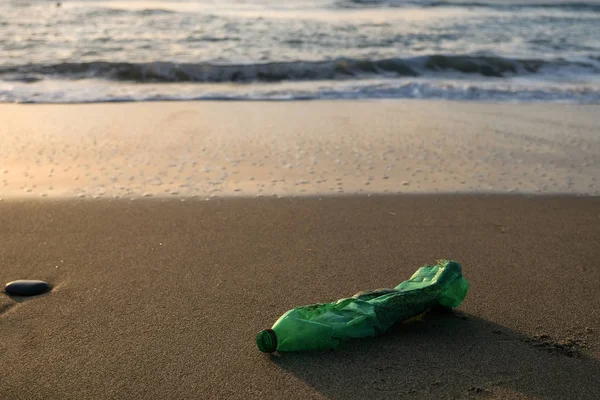 Grüne Plastikflasche an der Küste, Sonnenuntergang goldenes Licht, verschmutztes Ökosystem-Konzept — Stockfoto