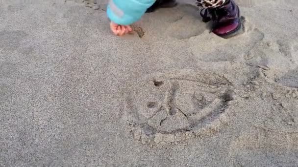 Liten söt barn flicka teckning leende ansikte i stranden sand, familj kärlek koncept — Stockvideo