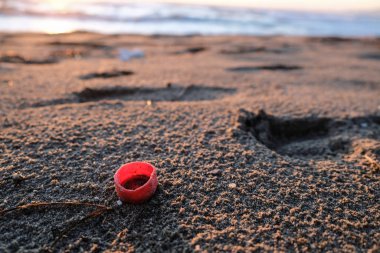 Günbatımı deniz kıyısında kırmızı plastik şişe mantarı, kirlenmiş ekosistem, mikroplastik