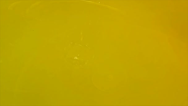 Singola goccia d'acqua rallentata da vicino su fondo giallo, superficie liquida — Video Stock