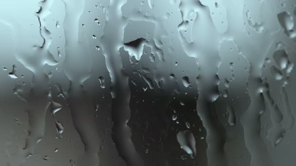 Gotas de agua de lluvia sobre vidrio sobre fondo azul borroso, movimiento líquido abstracto — Vídeos de Stock