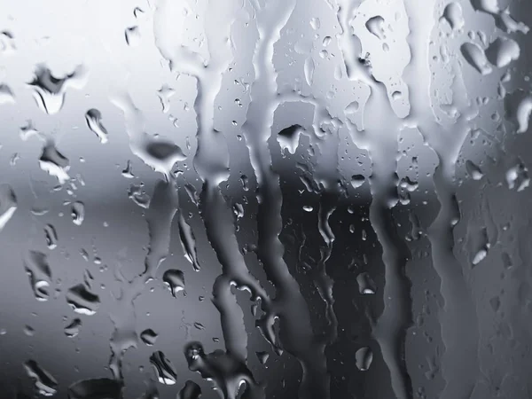 Gocce d'acqua piovana su vetro su sfondo argento sfocato, motivo astratto texture — Foto Stock