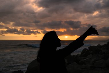 Genç kız silueti, gün batımında deniz ufkunda, Instagram sosyal medya iletişiminde selfie çektir. 