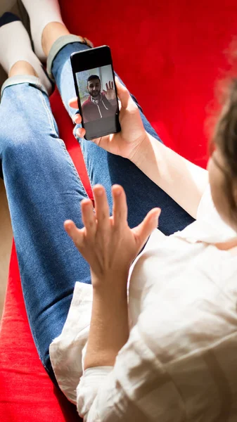 Τηλέφωνο βιντεοκλήση. Νεαρή γυναίκα μιλάει με το φίλο της με βιντεοκλήση, gesturing γεια σε αυτόν. Κορίτσι making facetime βίντεο καλώντας με smartphone που βρίσκεται στον καναπέ στο σπίτι. — Φωτογραφία Αρχείου