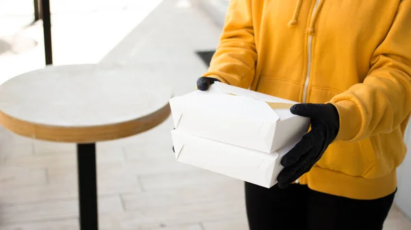 Kuryeyi paket kâğıt kutulara koyup paketleri paketle. Sarı üniformalı kız açık hava lokantasından yemek getiriyor.