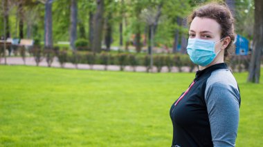 Spor, covid-19 sırasındaki aktif yaşam, karantina, koronavirüs. Sağlıklı aktif yaşam tarzı, yeşil çimlerin üzerinde duran koruyucu maskeli kadın. Esneme, açık havada koşma.