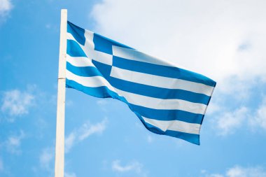 Yunanistan 'ın ulusal bayrağı mavi gökyüzünde beyaz bulutların altında. Rüzgarda dalgalanır. Güneşli bir günde bayrak direğinde Yunan bayrağı.