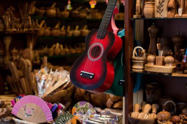 Sokak hatırası ahşap dükkanı. Geleneksel turistik hediyelik eşya pazarında asılı duran kırmızı tahta gitar. El fanı, ahşap baharat harcı, kaşıklar ve çatallar, Kerkyra, Korfu Adası, Yunanistan 