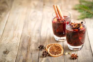 Elma, portakal, tarçın ve yıldız anasonlu cam bardaklarda sıcak şarap. Karanlık bir arka planda, köknar dalı fotokopi alanı olan sıcak Noel içeceği..