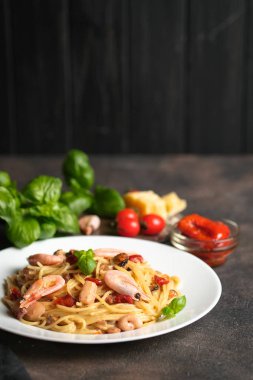 Deniz mahsullü makarna, güneşte kurutulmuş domates, parmesan ve fesleğen, arka planda açık bir tabakta, fotokopi alanı..
