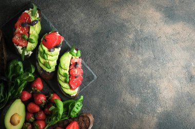 Sağlıklı yiyecekler. Vejetaryen kahvaltısı. Koyu arkaplan görünümlü avokado ve çilekli kızarmış ekmek veya tost..