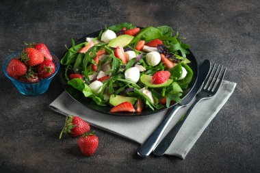 Taze çilekli salata, mozarella, tavuk, avokado ve koyu bir arka planda taze otlar..