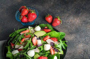 Taze çilekli salata, mozarella, tavuk, avokado ve koyu bir arka planda taze otlar..
