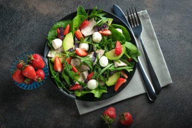 Taze çilekli salata, mozarella, tavuk, avokado ve koyu bir arka planda taze otlar..