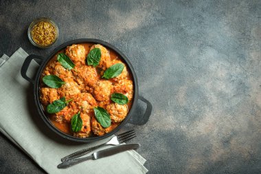 Koyu arkaplanda ıspanak yaprakları olan bir tavada köfte. Üst görünüm.