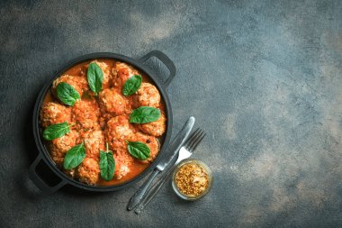 Koyu arkaplanda ıspanak yaprakları olan bir tavada köfte. Üst görünüm.