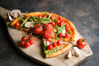 Geleneksel İtalyan pizzası, üzerinde kiraz domatesli, siyah arka planda tahta kürek..