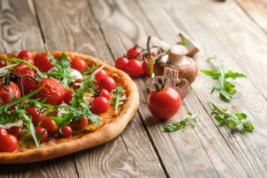 Geleneksel İtalyan pizzası, üzerinde kiraz domatesli, siyah arka planda tahta kürek..