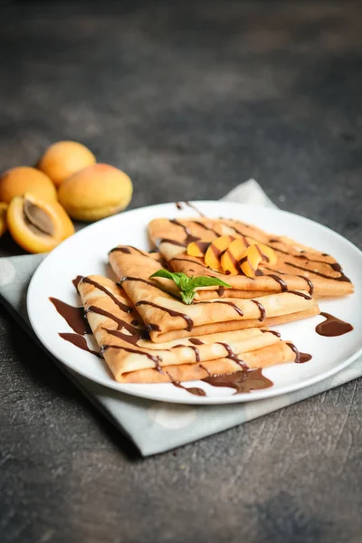 Crepes with chocolate sauce, fruits and mint on a dark background.