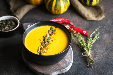 Kabak tohumlu ev yapımı balkabağı çorbası karanlık bir zeminde kabak kabağı, baharat ve otlarla fotokopi alanı..