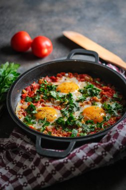 Geleneksel Shakshuka, yumurta, domates ve maydanozlu, siyah arka planda demir bir tavada. 