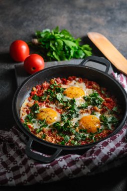 Geleneksel Shakshuka, yumurta, domates ve maydanozlu, siyah arka planda demir bir tavada. 