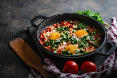 Geleneksel Shakshuka, yumurta, domates ve maydanozlu, siyah arka planda demir bir tavada. 