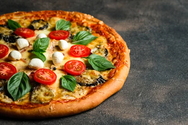 Traditional Italian pizza with eggplants, mozzarella, basil and tomatoes on a dark background copy space.