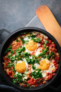 Geleneksel shakshuka ile yumurta, domates ve maydanozu siyah arka planda demir bir tavada. Üst görünüm.