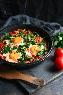 Geleneksel Shakshuka, yumurta, domates ve maydanozlu, siyah arka planda demir bir tavada. 