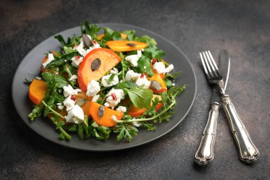 Sağlıklı salata, hurma, roka, beyaz peynir ve kabak tohumları koyu bir arka planda. Vejetaryen menüsü, sağlıklı yiyecekler. Vitamin eksikliğinin önlenmesi. 