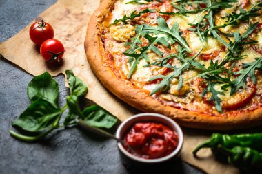 Geleneksel İtalyan pizzası jambon, roka, mozzarella, fesleğen ve domatesli koyu arka planda fotokopi alanı..