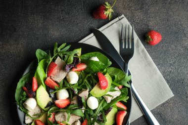 Taze çilekli salata, roka, fesleğen, avokado ve koyu arkaplanda mozzarella. Sağlıklı vejetaryen kahvaltısı. Üst Manzara. Boşluğu kopyala.