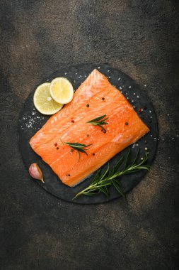 Bitki, limon, biberiye ve baharatlı taze somon bifteği kesme tahtasının üzerinde koyu bir arka plan manzarası var.