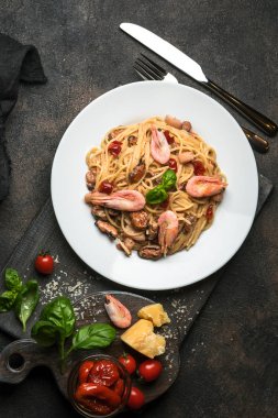Deniz ürünleri makarnası. Karidesli bir tabak spagetti, kurutulmuş domates, fesleğen ve koyu arkaplanlı parmesan. Boşluğu kopyala.