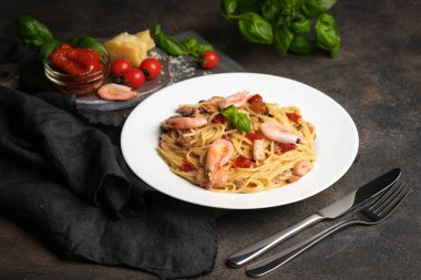 Deniz ürünleri makarnası. Karidesli bir tabak spagetti, kurutulmuş domates, fesleğen ve koyu arkaplanlı parmesan. Boşluğu kopyala.