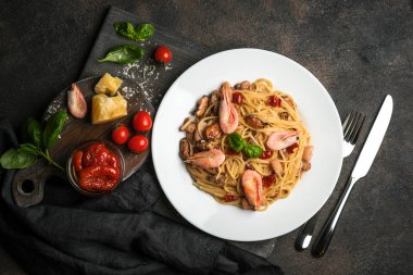 Deniz ürünleri makarnası. Karidesli bir tabak spagetti, kurutulmuş domates, fesleğen ve koyu arkaplanlı parmesan. Boşluğu kopyala.