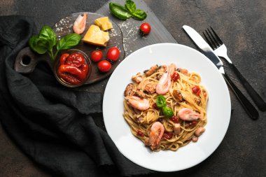 Deniz ürünleri makarnası. Karidesli bir tabak spagetti, kurutulmuş domates, fesleğen ve koyu arkaplanlı parmesan. Boşluğu kopyala.