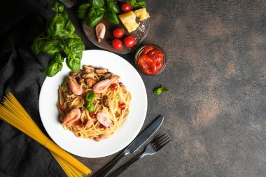 Deniz ürünleri makarnası. Karidesli bir tabak spagetti, kurutulmuş domates, fesleğen ve koyu arkaplanlı parmesan. Boşluğu kopyala.