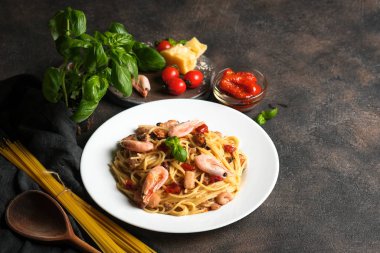 Deniz ürünleri makarnası. Karidesli bir tabak spagetti, kurutulmuş domates, fesleğen ve koyu arkaplanlı parmesan. Boşluğu kopyala.