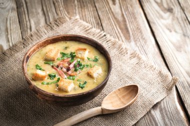 Domuz pastırmalı bezelye çorbası, otlar ve kırsal kasede ekmek kırıntıları ve ahşap arka planda fotokopi alanı.