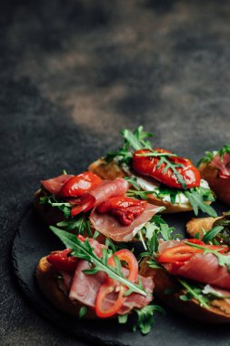 Geleneksel İtalyan bruschetta domatesli, prosciutto, krem peynirli ve roka kaplı koyu renkli bir fonda.