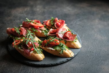 Geleneksel İtalyan bruschetta domatesli, prosciutto, krem peynirli ve roka kaplı koyu renkli bir fonda.