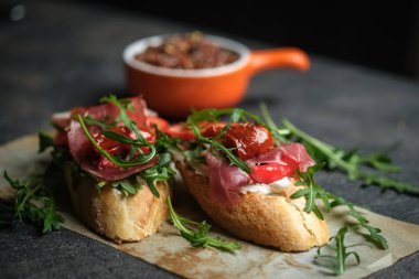 Geleneksel İtalyan bruschetta domatesli, prosciutto, krem peynirli ve roka kaplı koyu renkli bir fonda.