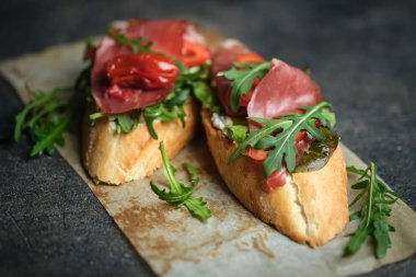 Geleneksel İtalyan bruschetta domatesli, prosciutto, krem peynirli ve roka kaplı koyu renkli bir fonda.